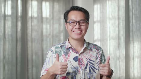 카드보드 상자를 가진 아시아 남자의 근접 사진 웃음과 엄지손가락을 보여주는 새로운 집에서 카메라에 대한 제스처
