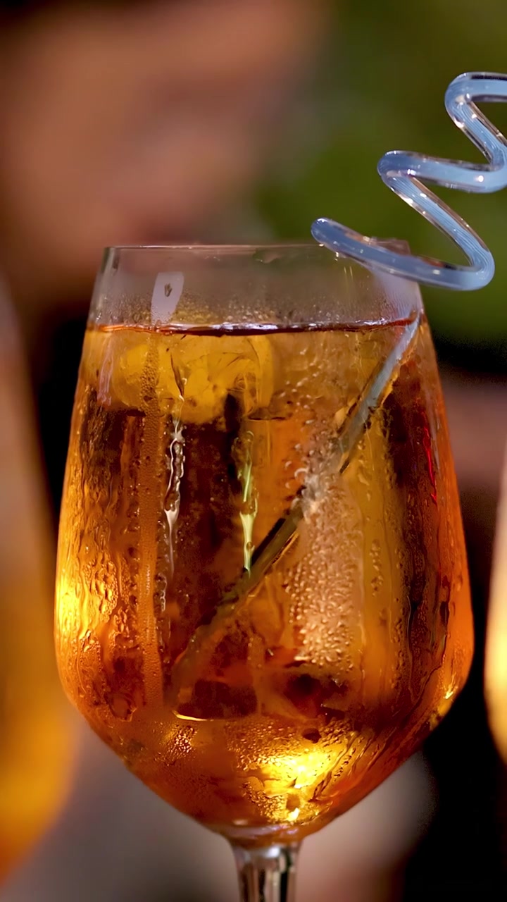 Primo piano di un cocktail Negroni con cannuccia a spirale, ghiaccio, condensa e illuminazione esterna serale, panoramica lenta