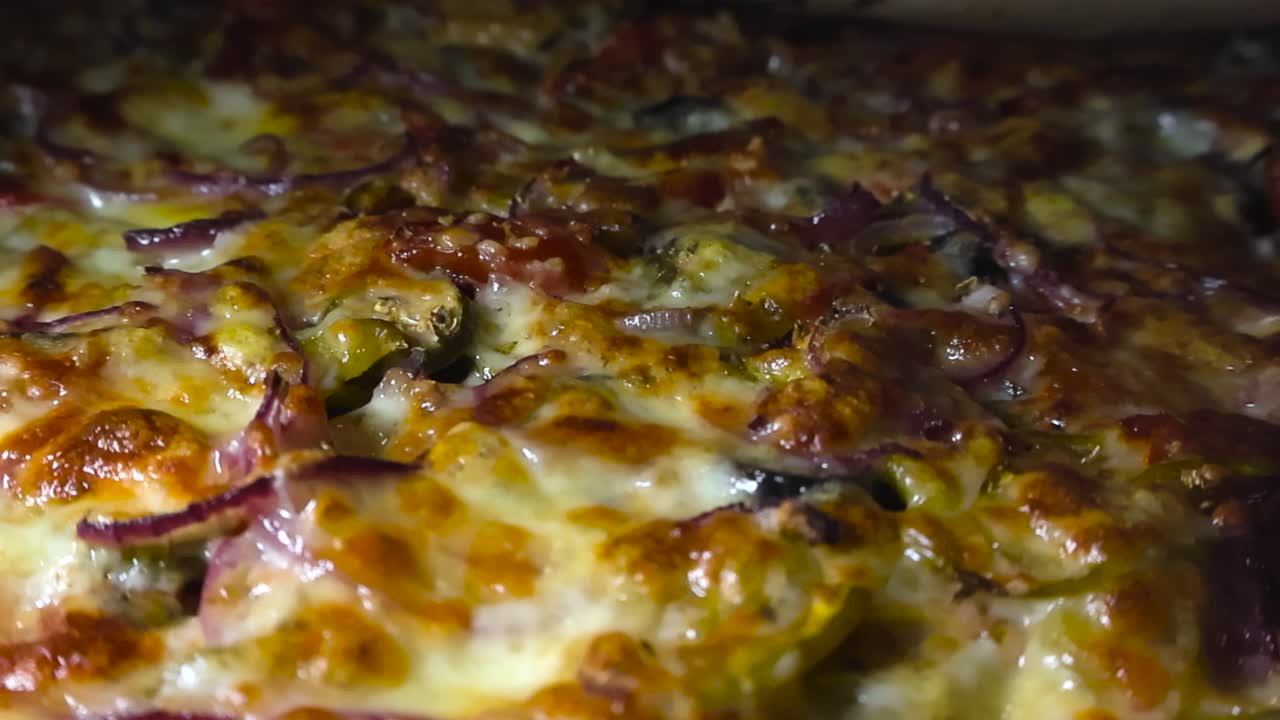 Close up view of grilled golden yellow and brown colored cheese and pizza toppings on a homemade pizza where steaming hot tomatoes, sauce, jalapenos, onions and meat is visible in the cheese