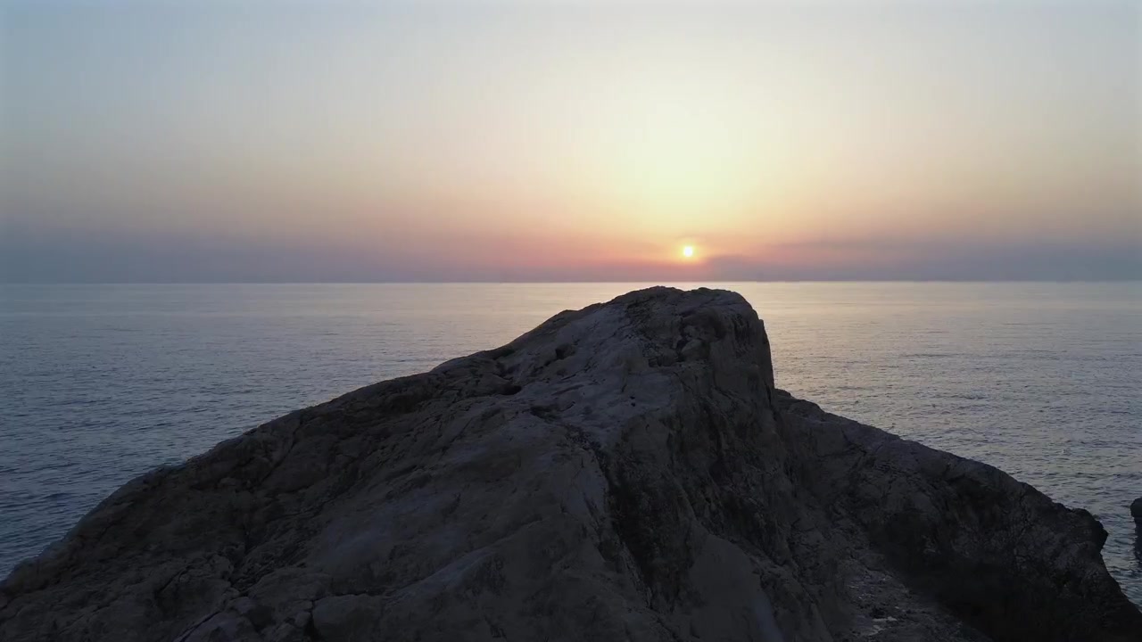 Smuk droneoptagelse i lav vinkel, der fanger en gylden solnedgang over den rolige havhorisont ved Kathisma strand, Lefkada. Med massive klippeblokke i silhuet og varme solstråler, stemningsfuld aftentid.