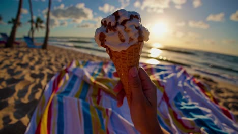 POV shot of a hand holding an ice cream cone on a beach at sunset