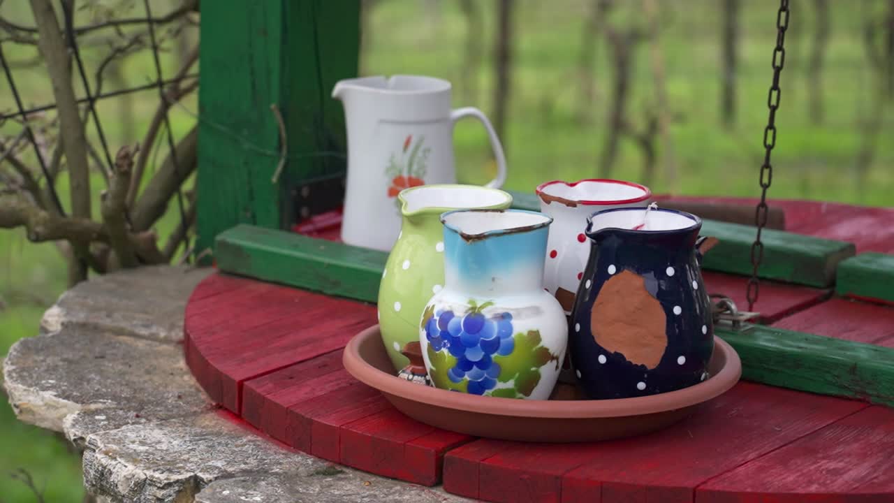Colorful ceramic jugs on a red wooden well with green frame