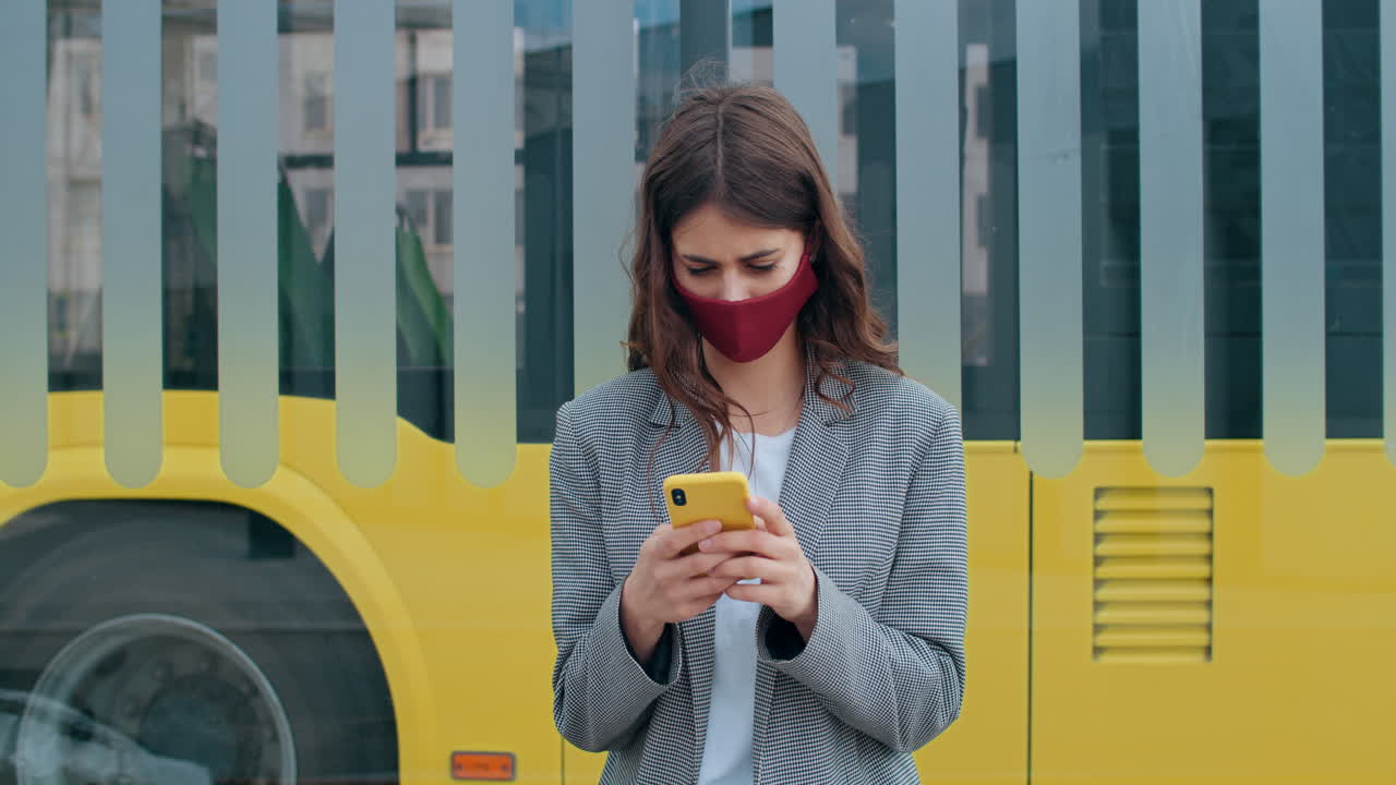 Young woman wearing a face mask using smartphone at a bus stop