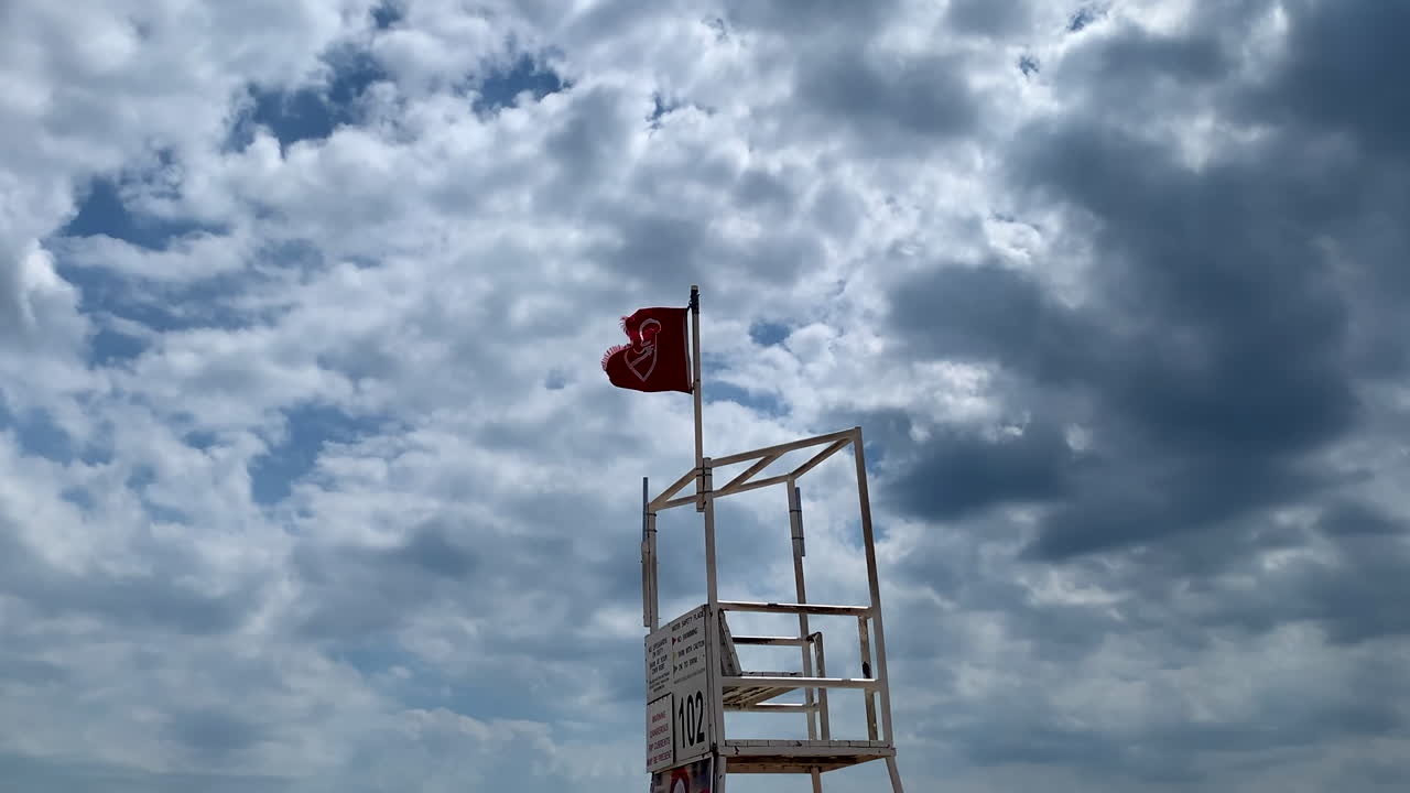 Red flag on lifeguard chair against cloudy sky