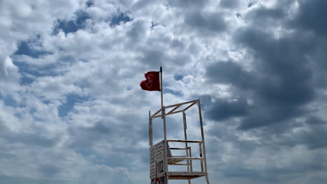 red flag on lifeguard chair against cloudy sky