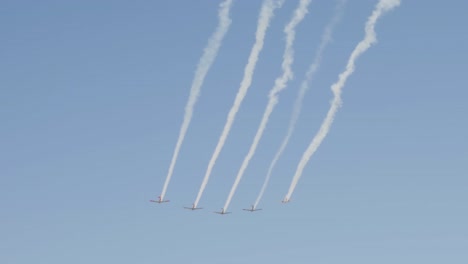 five vintage war planes fly in formation leaving contrails behind in the blue sky