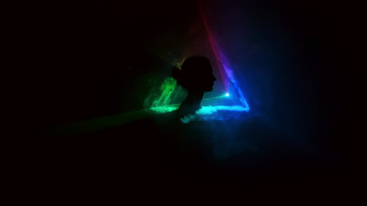 imagen de una niña en un fondo claro de diferentes colores moviéndose en la oscuridad. el humo llena el triángulo con la cabeza de la niña. proyector.