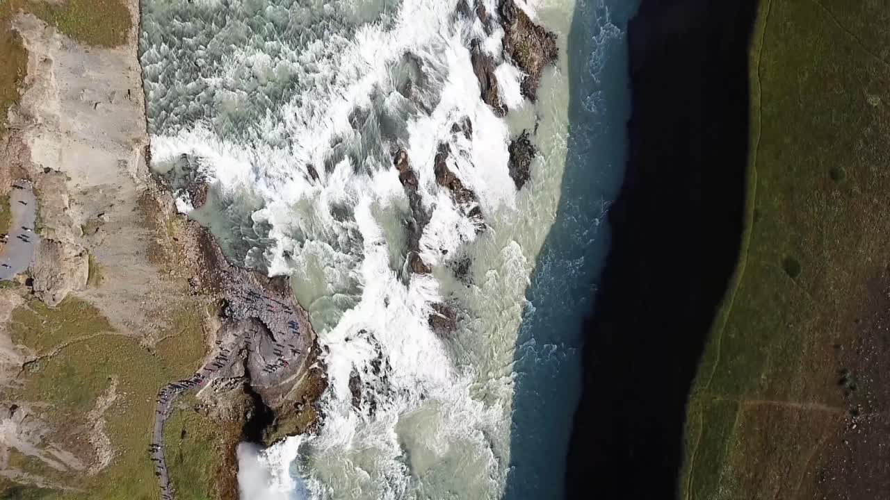 Stunning aerial view of Gullfoss Waterfall in Iceland, showcasing its dramatic cascades, rugged terrain, and powerful water flow surrounded by lush greenery and pathways carved into the landscape