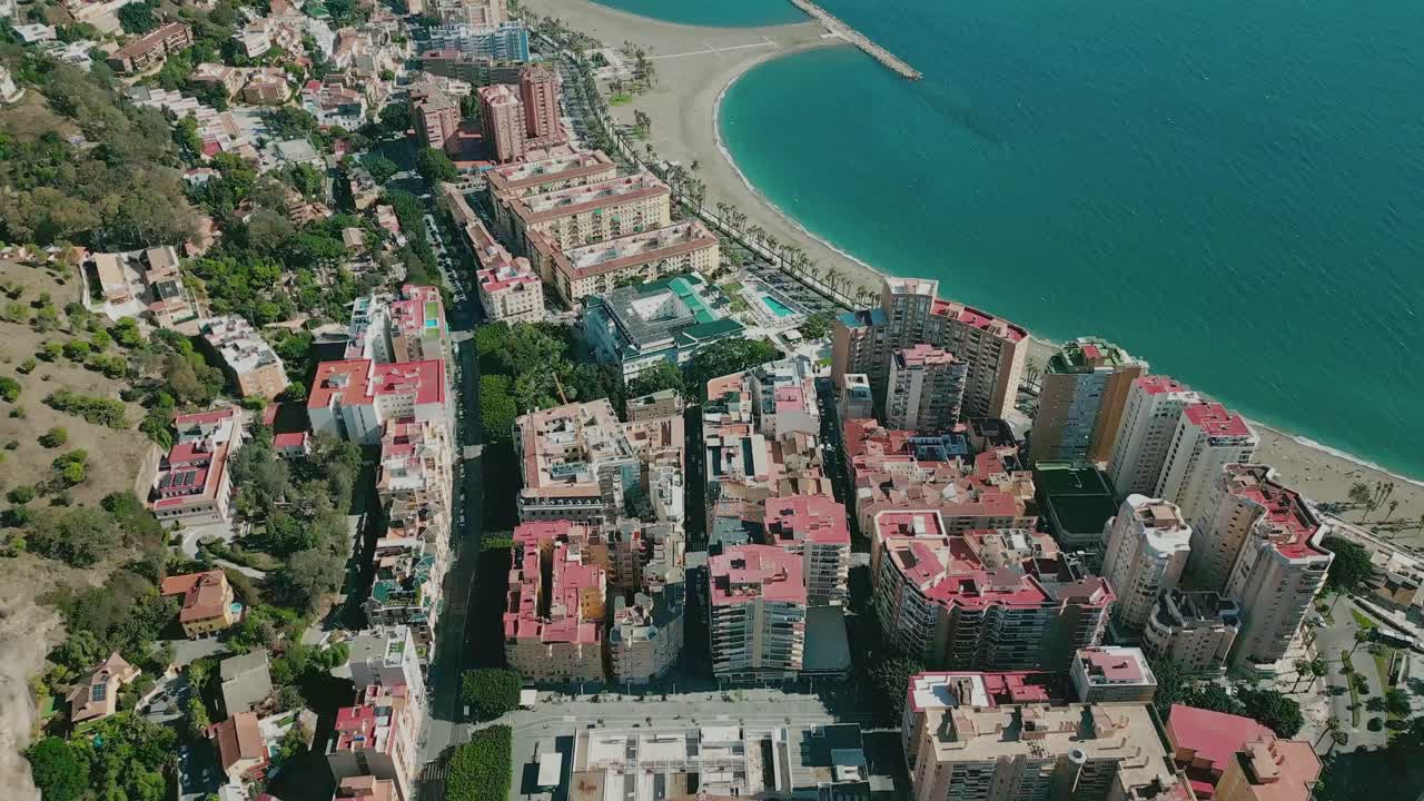 Aerial view of Playa de la Malagueta with calm waves, sunlit city, and historic Málaga Bullring in frame, Andalusia, Spain