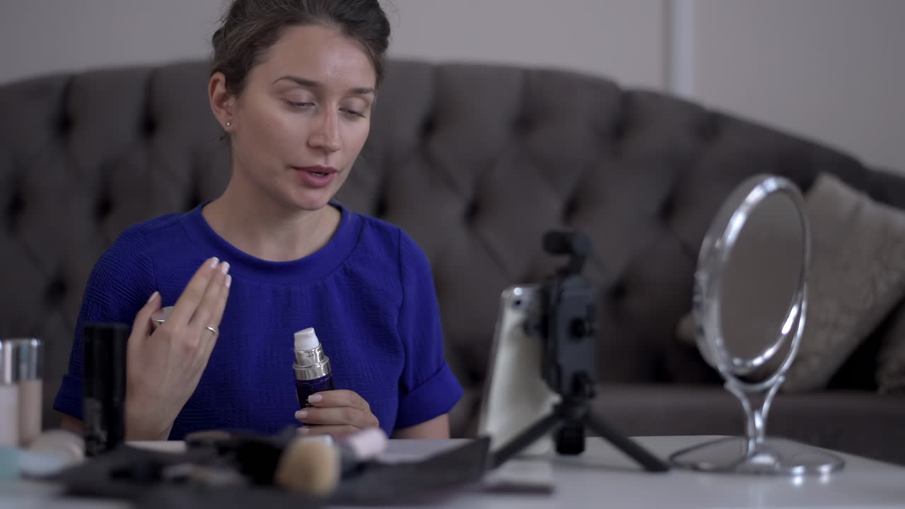 Woman in a blue T-shirt filming herself while doing a make-up tutorial at home