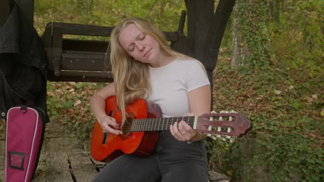 Happy-singer-songwriter-female-guitar-rehearses-by-forest-wishing-well