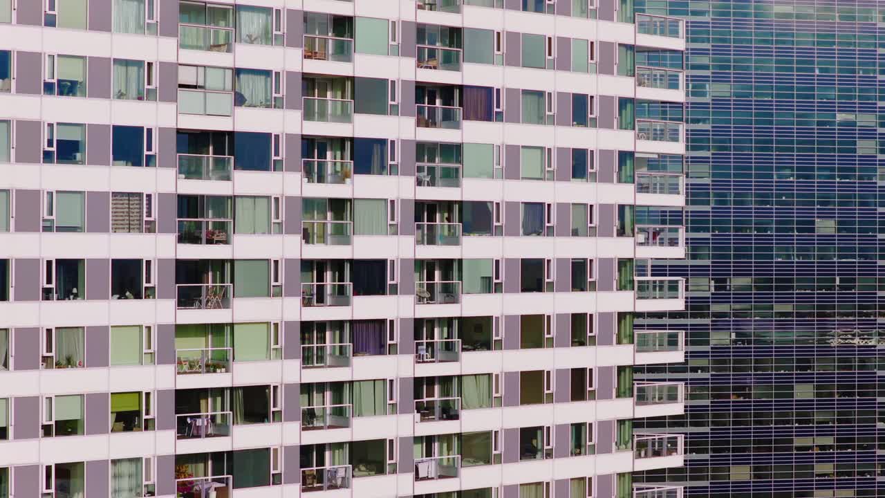 Vista detalhada de dois edifícios altos com fachadas contrastantes: varandas residenciais de um lado e janelas de escritório com painéis de vidro do outro, mostrando a arquitetura urbana