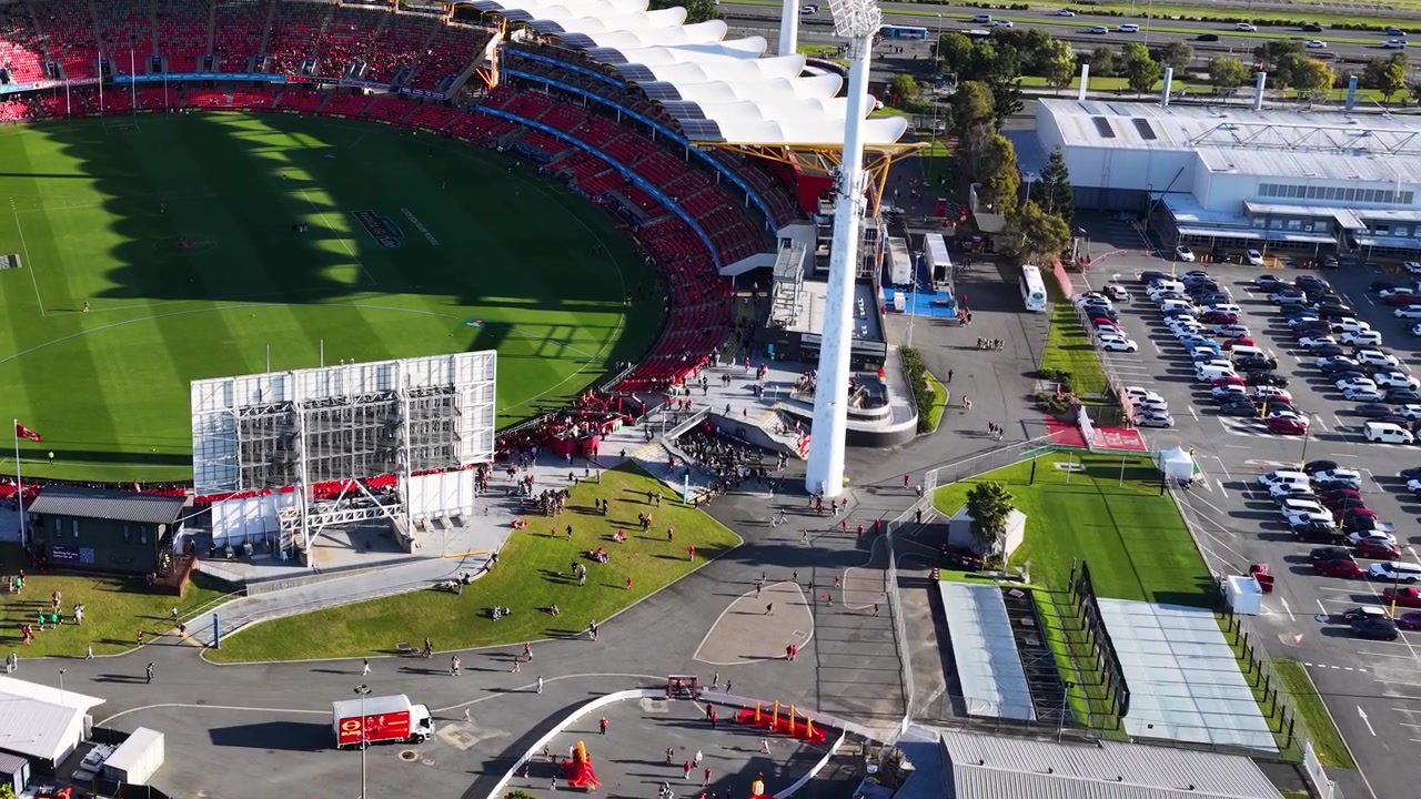 Tomada de drone em ângulo alto captura uma grande arena esportiva com campo verde e infraestrutura de estacionamento ao redor
