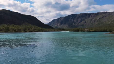 vue aérienne du ruisseau de montagne coule à travers une vallée verte luxuriante avec des sommets de montagnes escarpés en arrière-plan, le tout sous un ciel parsemé de nuages par une journée lumineuse