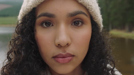 close up portrait beautiful mixed race woman looking serious expression wearing beanie for cold winter outdoors in nature by lake