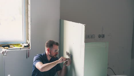 electrician fixes plug on wall using screwdriver in room