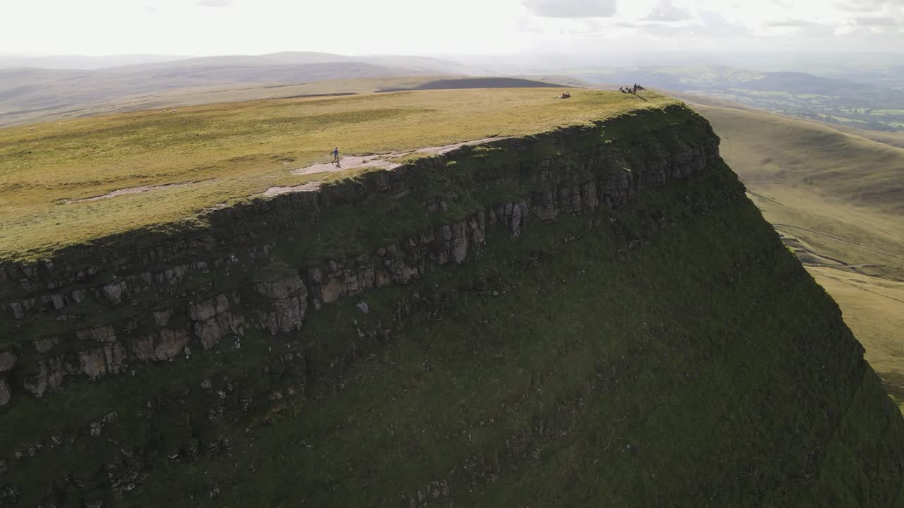 la gente caminando por el parque nacional de brecon beacons, la vista aérea de la cordillera revela un idílico y brillante lago del valle azul