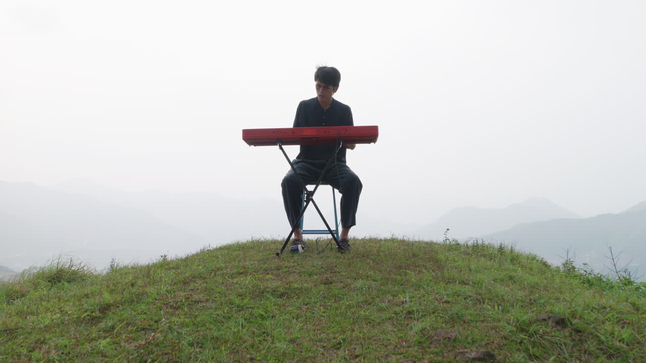 안개가 많은 언덕 꼭대기에 앉아 피아노를 연주하는 아시아의 젊은 남자