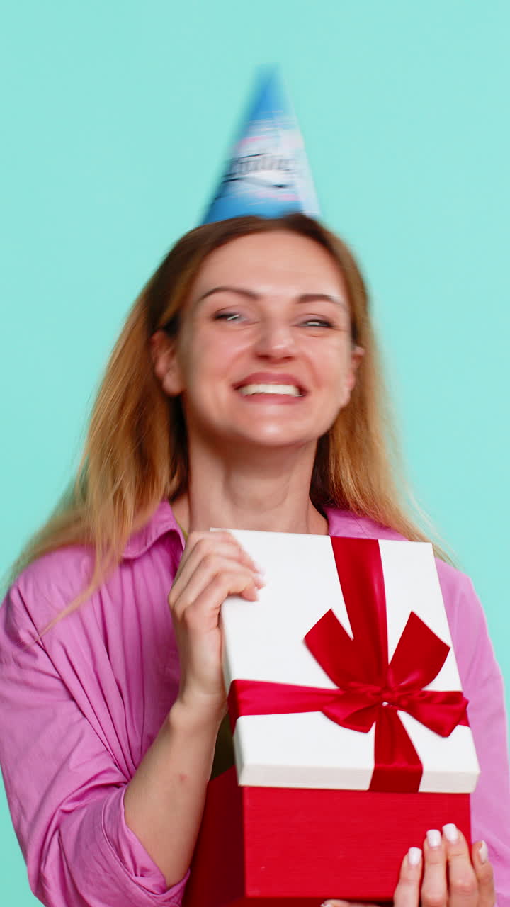 Adult woman celebrating birthday in party hat receiving gift and expressing happiness with big smile