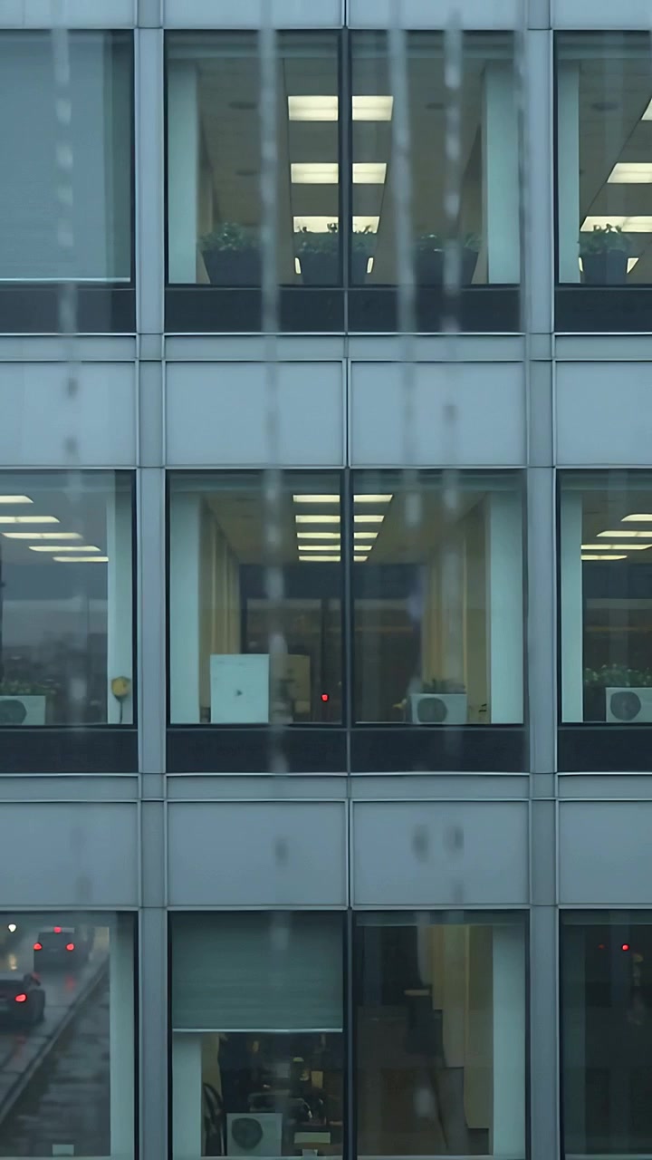 Video verticale: pioggia che cade causando lo scivolamento di gocce centrali lungo una finestra in ufficio
