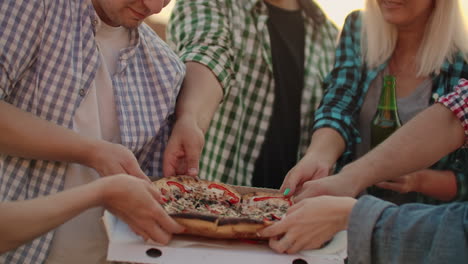 Un-Grupo-De-Seis-Jóvenes-Rusos-Cortan-Trozos-De-Pizza-Caliente-Y-Comen-Juntos.-Esta-Es-Una-Fiesta-En-La-Azotea-Con-Una-Cerveza.