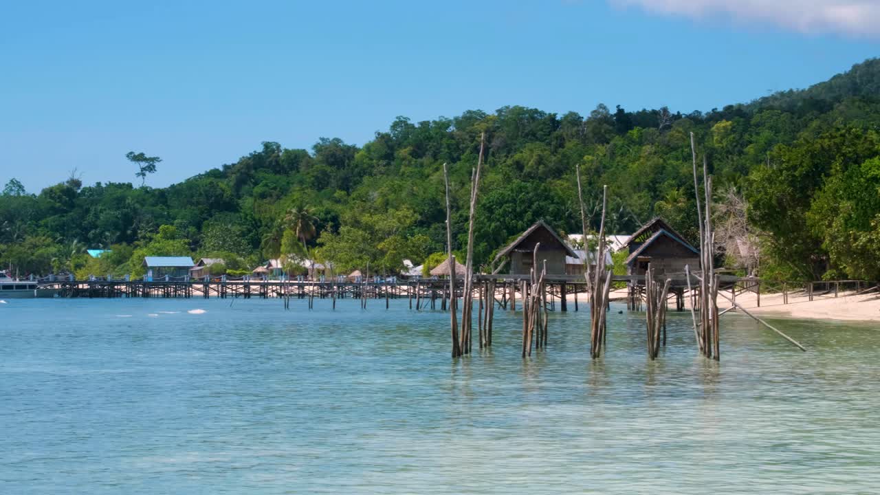 Endonezya'nın Batı Papua bölgesindeki Raja Ampat'ta, yağmur ormanı ağaçlarıyla kaplı bir adada, beyaz kumlu plajı ve turkuaz okyanus suyuna bakan ahşap plaj kulübeleri bulunan manzaralı egzotik tropikal adanın yavaş kaydırma çekimi.
