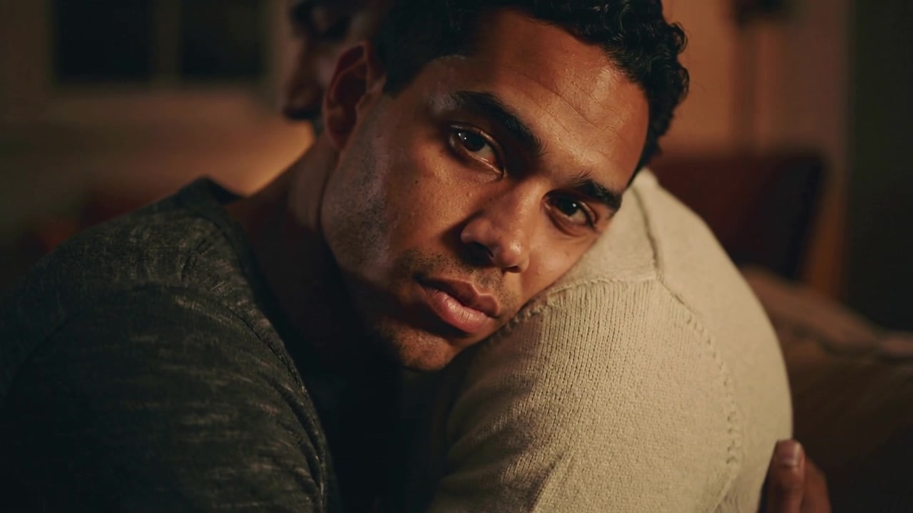 Looking man in plain dark tee, holding partner on couch, camera moving closer seeking comfort