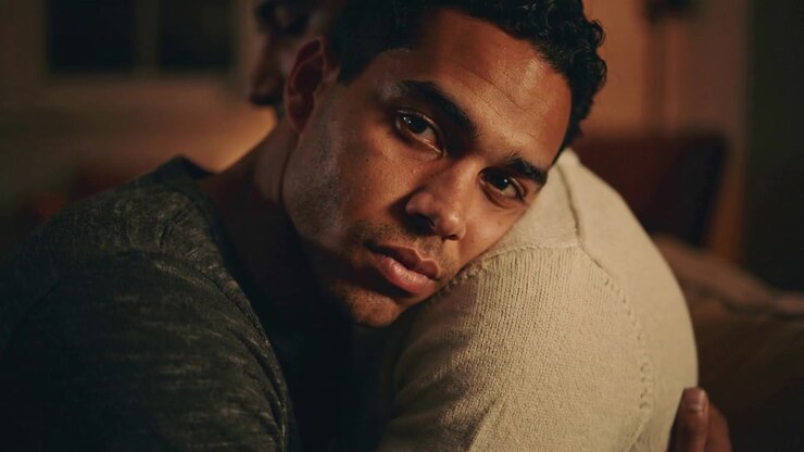 Looking man in plain dark tee, holding partner on couch, camera moving closer seeking comfort
