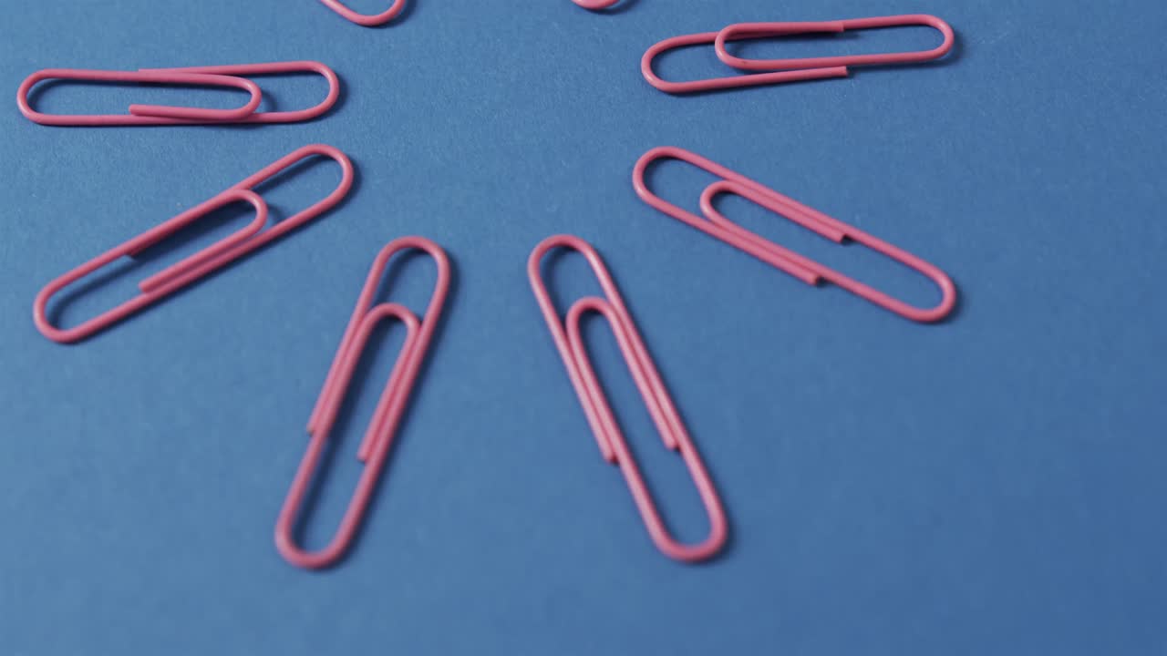 Close up of pink paper clips arranged on blue background, in slow motion