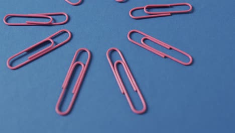 close up of pink paper clips arranged on blue background, in slow motion