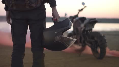 el motociclista irreconocible se para, mirando su bicicleta mientras el motor está funcionando y soplando humo de escape de color, holi