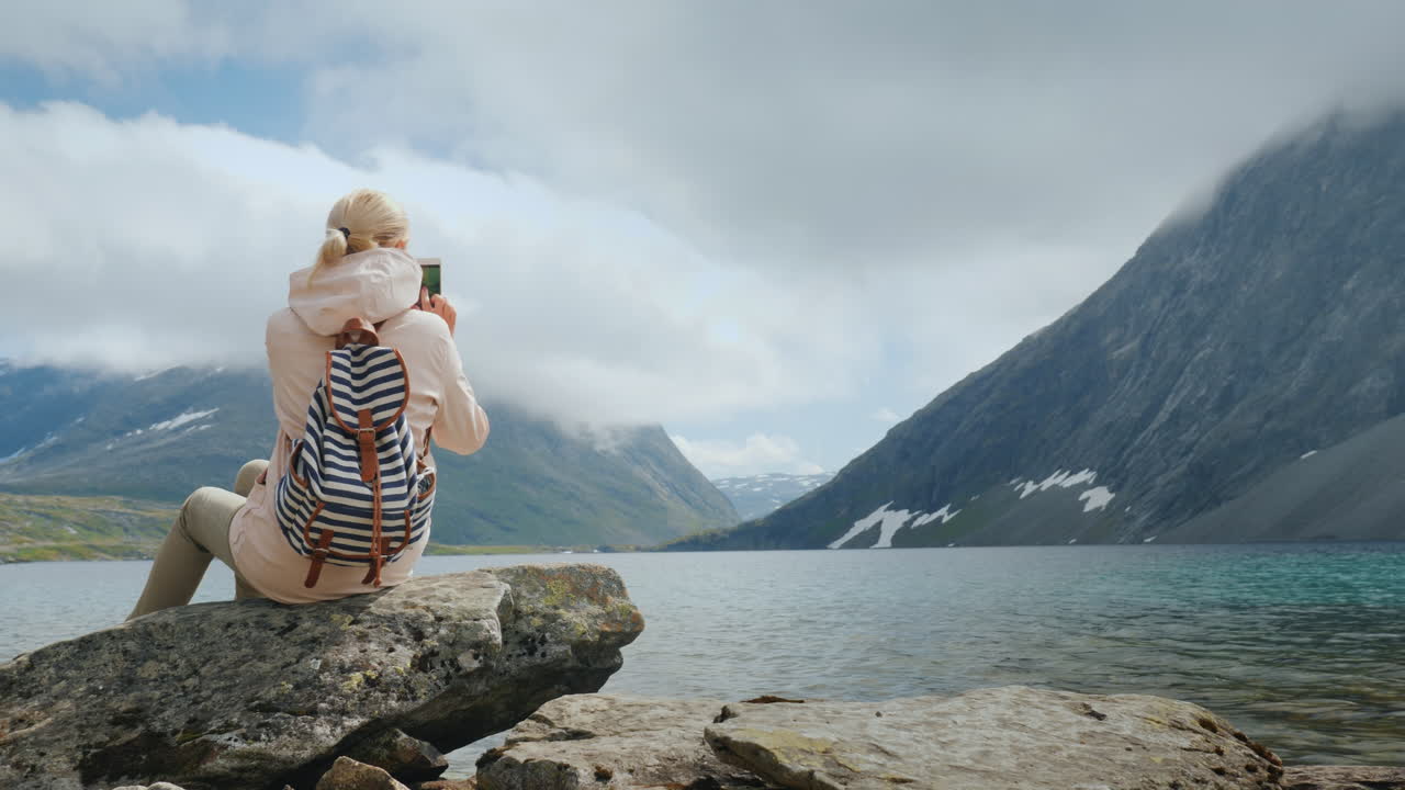 una mujer toma una foto de una vista panorámica de un lago noruego de alta montaña vacaciones en el borde o