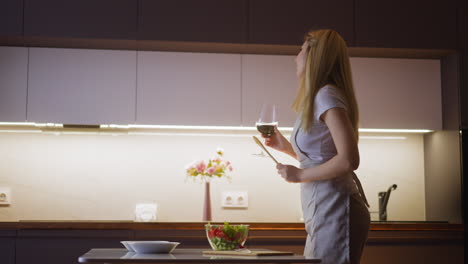 lady with spoon and glass of wine dances by table with salad