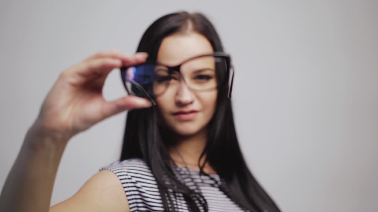 Attractive young woman in stylish eyeglasses removes them to the camera close-up. Pretty female with glasses for vision on the grey background.