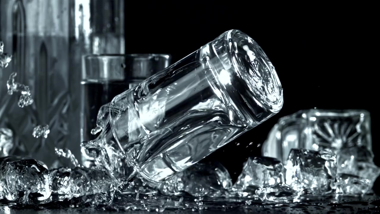 Shotglas falder og sprøjter vand med isterninger i slowmotion