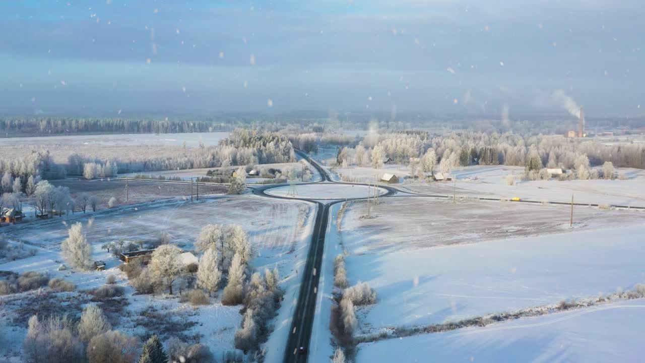 Talvinen liikenneympyrä yhdistää lumipeitteiset pellot ja huurteiset puut aurinkoisena aamuna ilmasta kuvattuna lumisateen kera