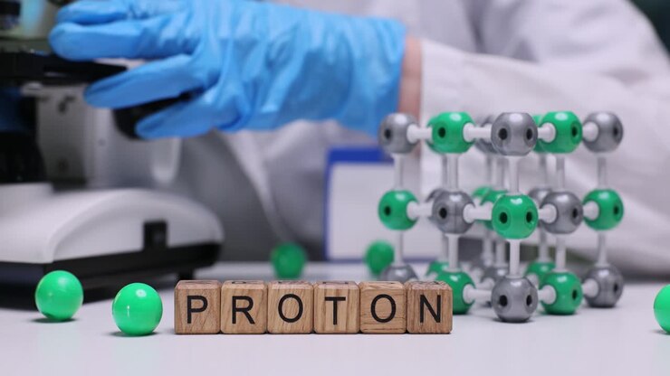 Blocchi di legno formano la parola 'protone' accanto a un modello molecolare e strumenti da laboratorio.