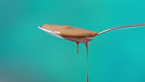 close up of melted chocolate dripping from overflowing spoon against blue coloured background with copy space 2