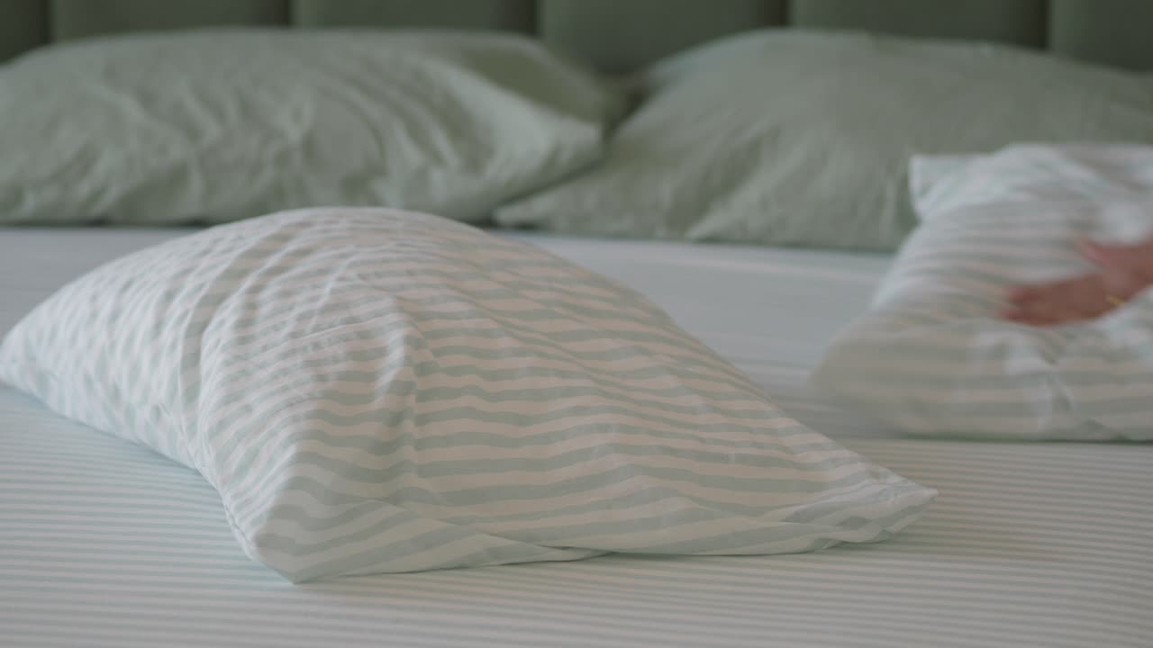 Woman's Hand Arranging Pillows on a Striped Bed