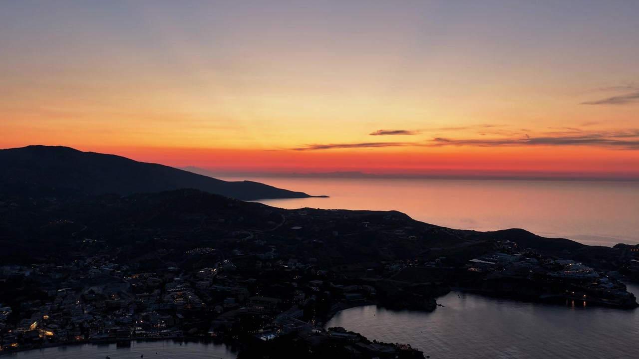 Timelapse aerial drone view of the coastline and headlands with scattered town lights under a red afterglow, Agia Pelagia, Greece