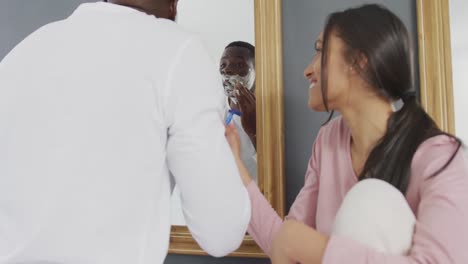 Video-of-happy-diverse-couple-having-fun,-laughing-in-bathroom-while-man-shaves
