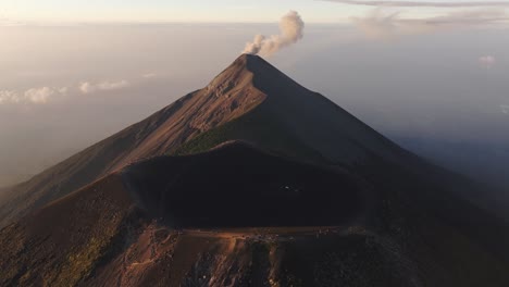 aerial tilt shot in front of a huge crater with smoking fuego volcano background