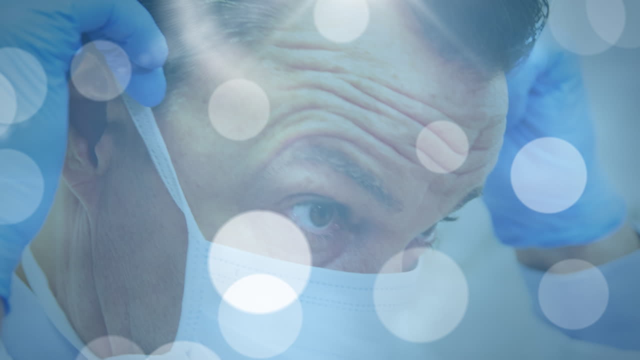 얼굴 마스크를 쓰고 있는 백인 남성 의사 위의 빛 반점의 애니메이션