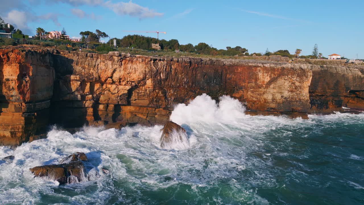 Drone rugged coastal rocks washing by ocean waves. Sea water breaking on cliffs.
