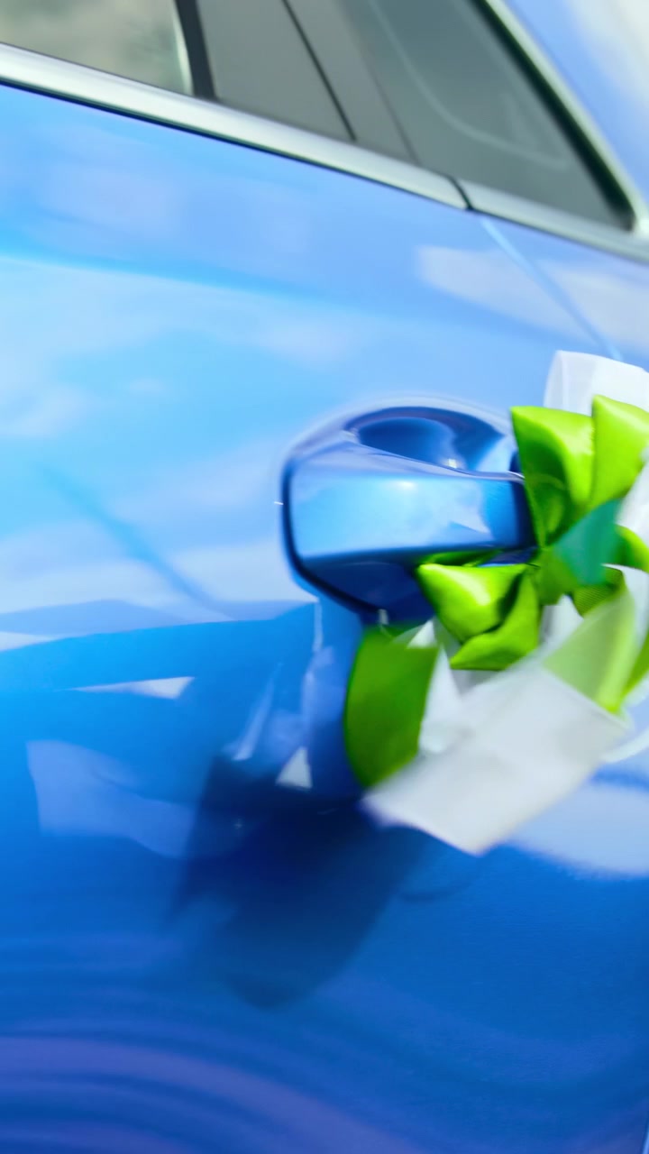 Auto blu decorata con fiocco a nastro verde sulla maniglia della portiera, vernice metallizzata lucida che riflette il cielo, matrimonio festivo