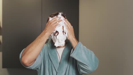 a man rubs shaving foam on his face while standing in the bathroom