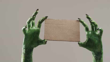 Video-Von-Halloween-grünen-Monsterhänden,-Die-Eine-Karte-Mit-Kopierraum-Auf-Grauem-Hintergrund-Halten