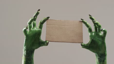 video of halloween green monster hands holding card with copy space on grey background