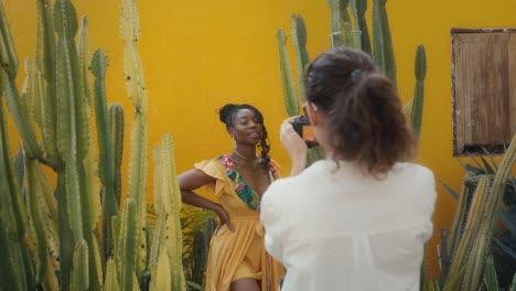 woman being photographed in a garden with cacti and a yellow wall