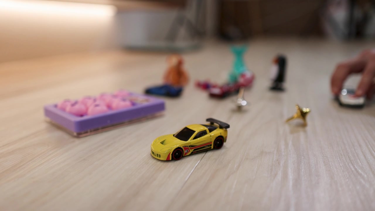 Close-up of a yellow toy car with miniature figures on a light wooden floor.
